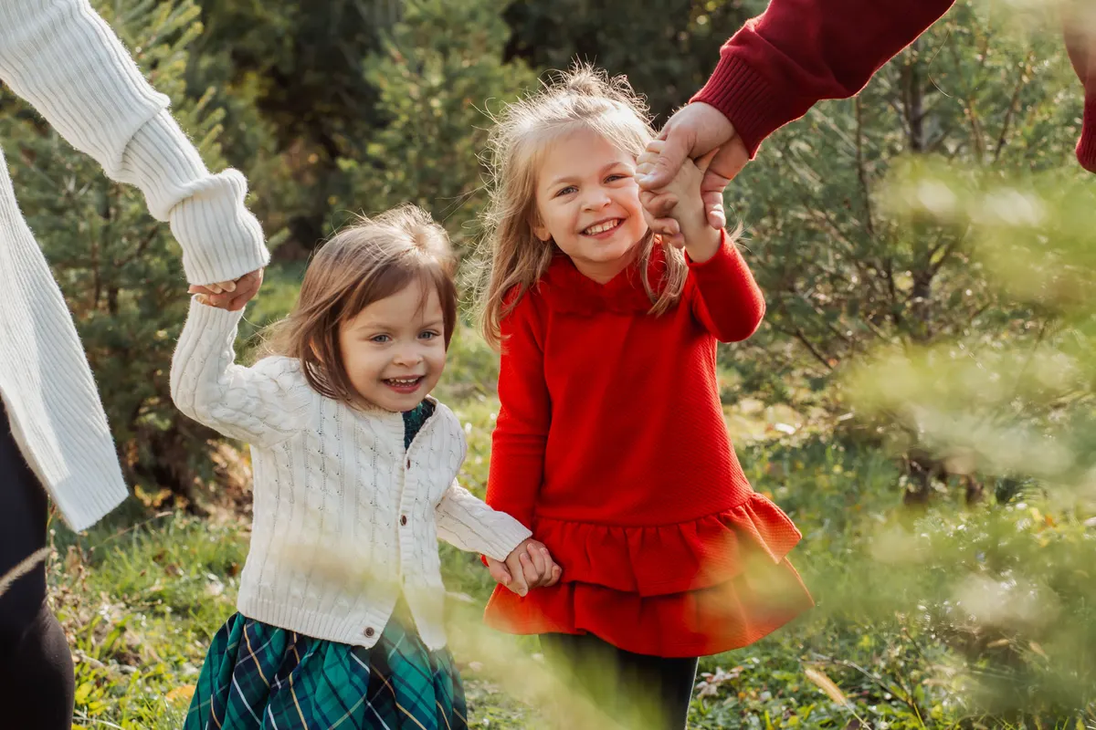 Two little girls in holiday dresses holding hands at a Christmas tree farm