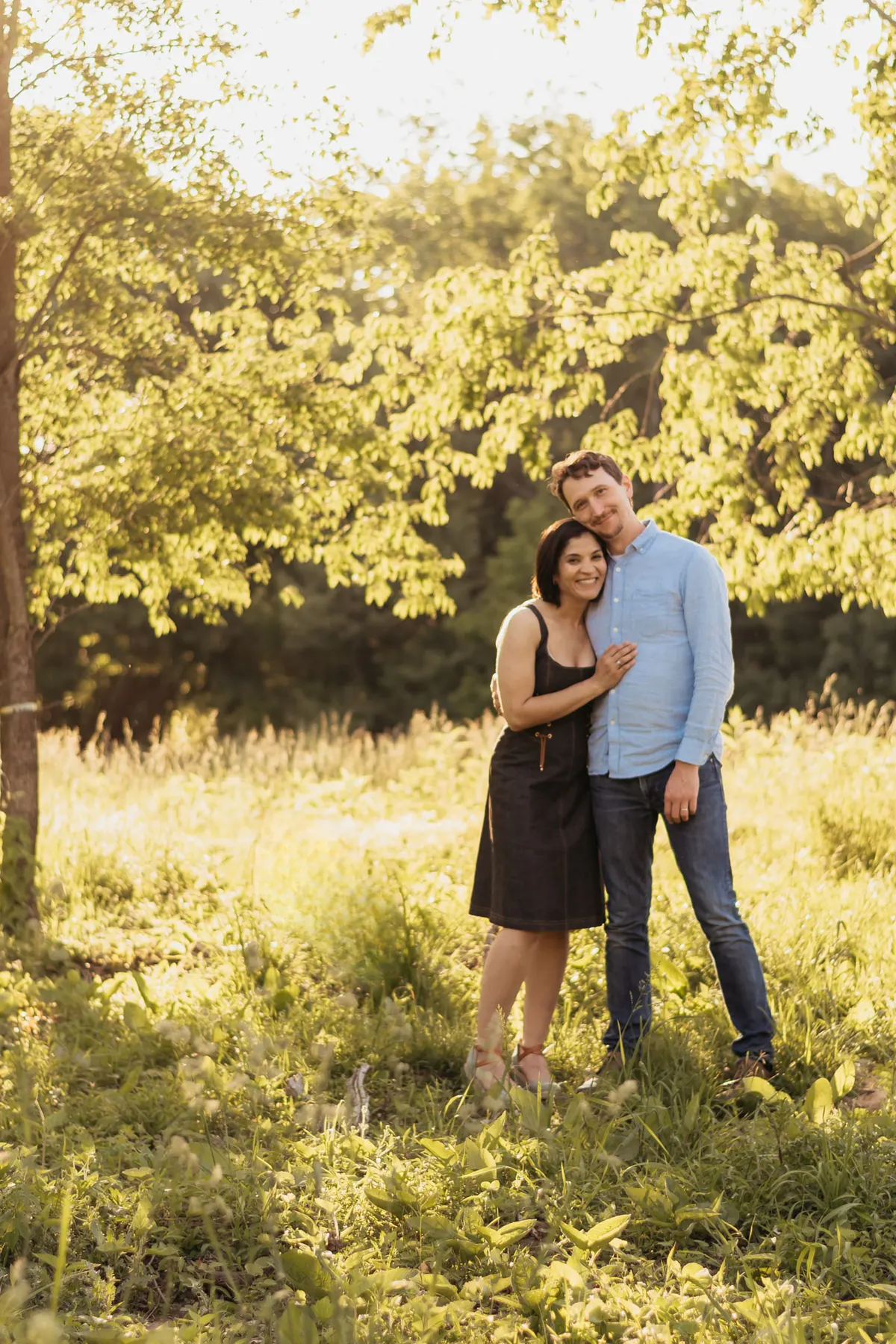 Couple hugging in a golden meadow under backlit trees