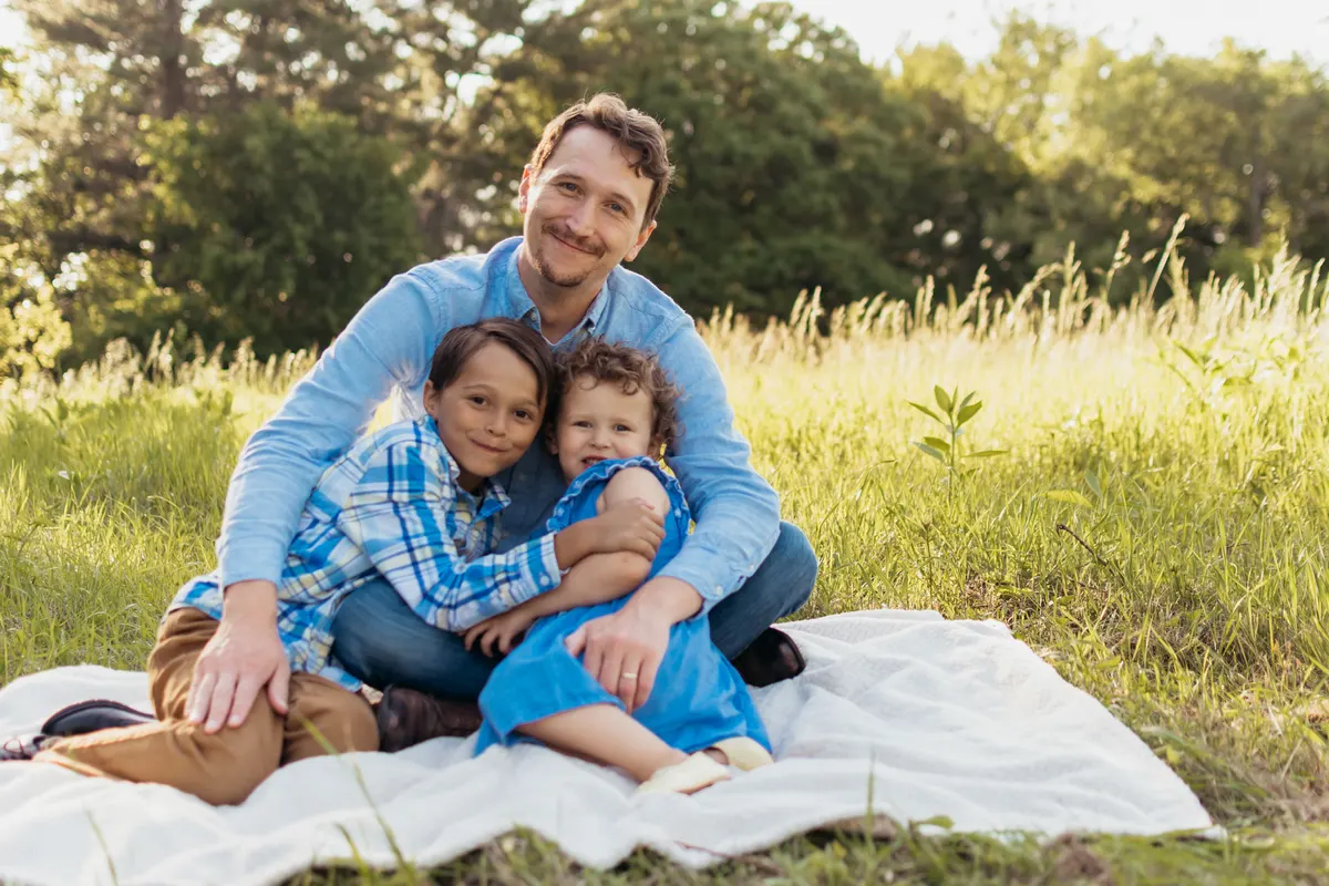 Dad hugging his two kids on a blanket in a meadow