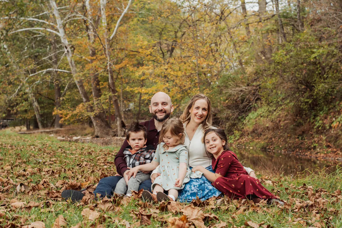 Family of five sitting together in fall leaves beside the creek at Mingo Creek Park