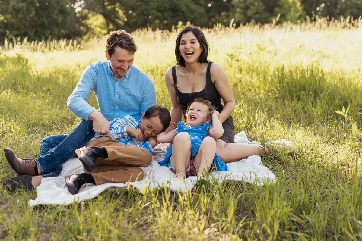 Parents and two kids laughing together on a blanket in a sunlit meadow during a Pittsburgh family photo session