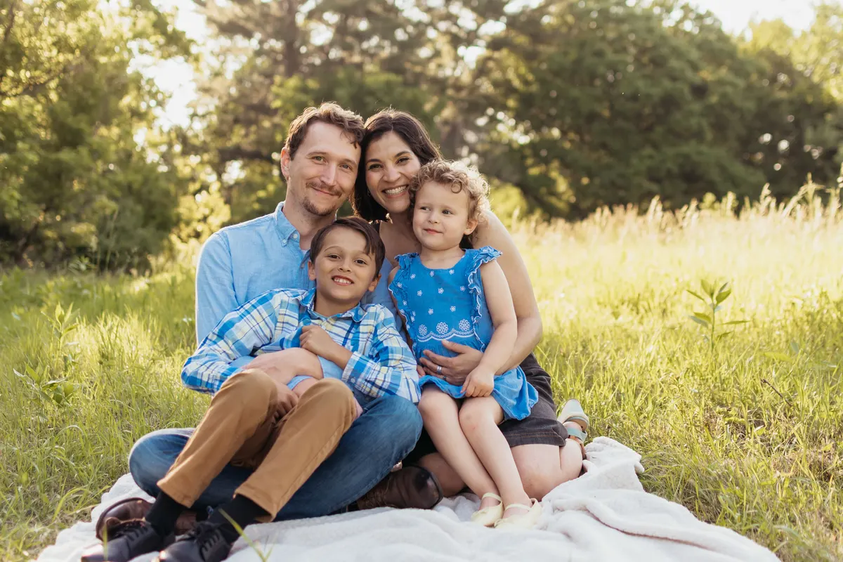 Family of four snuggled together on a blanket in a meadow at golden hour