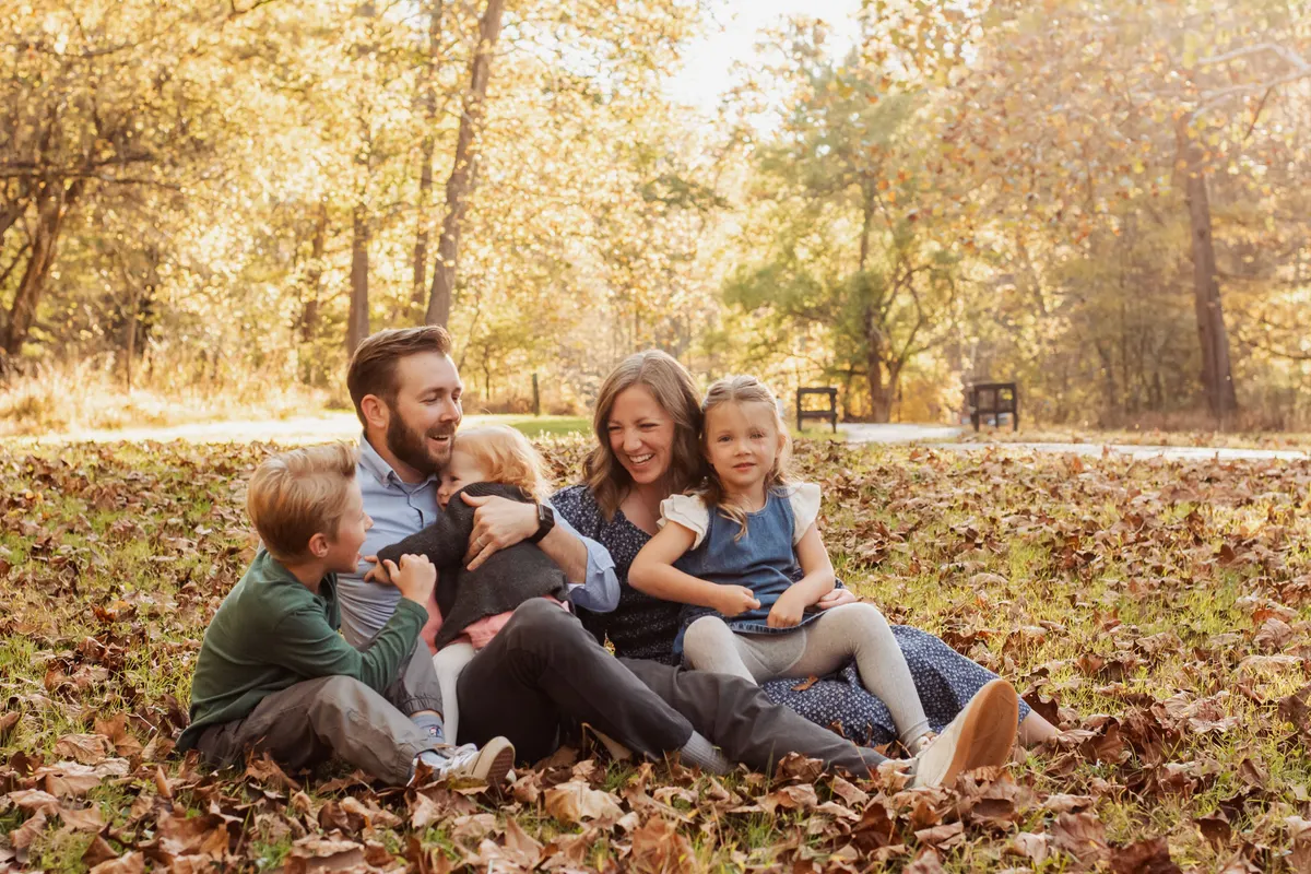 Family of four sitting and laughing in fall leaves