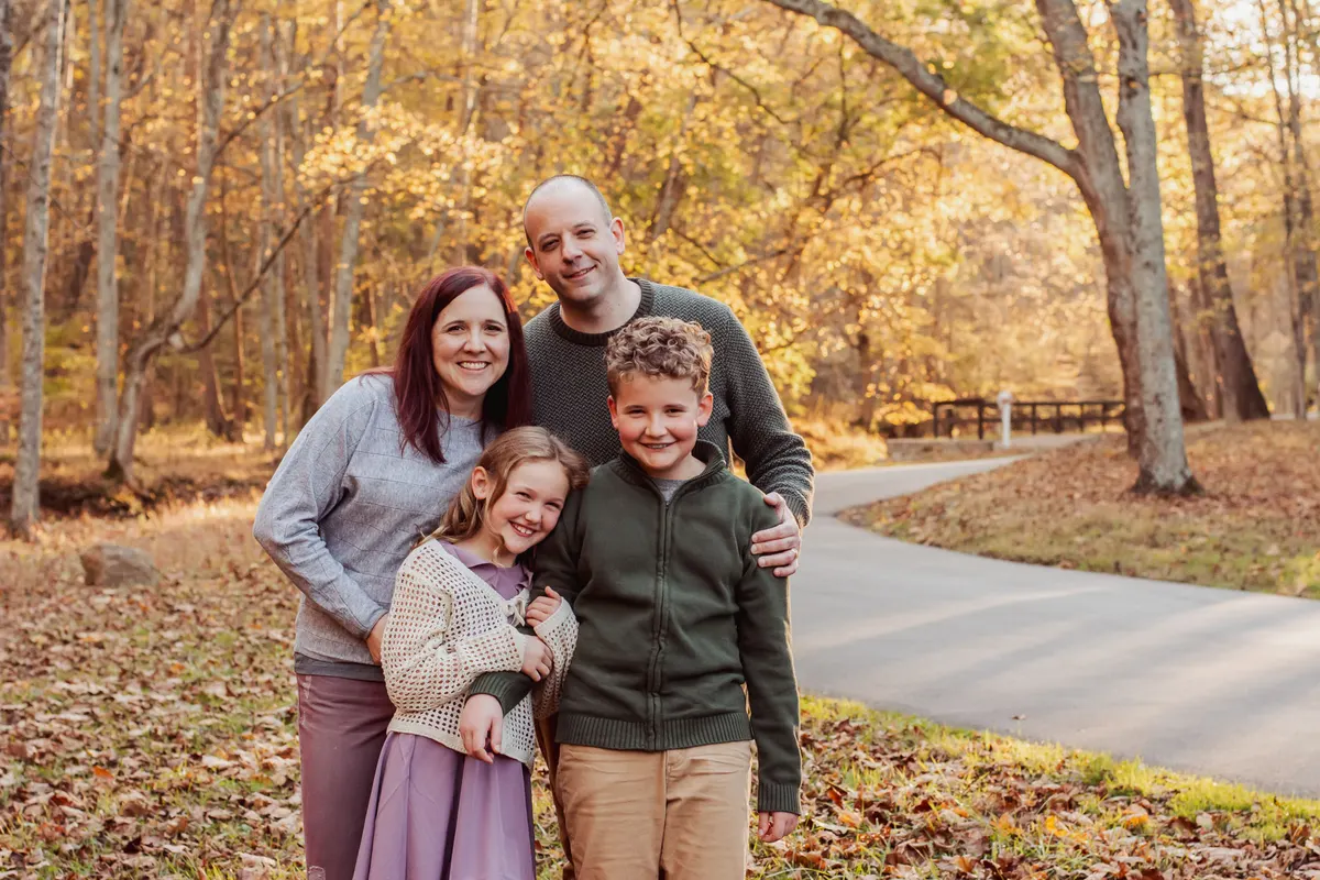 Family of four standing together beside a park path in fall color at Mingo Creek