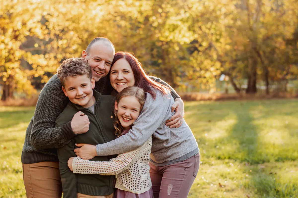 Family of four in a big group hug in golden fall light at Mingo Creek Park
