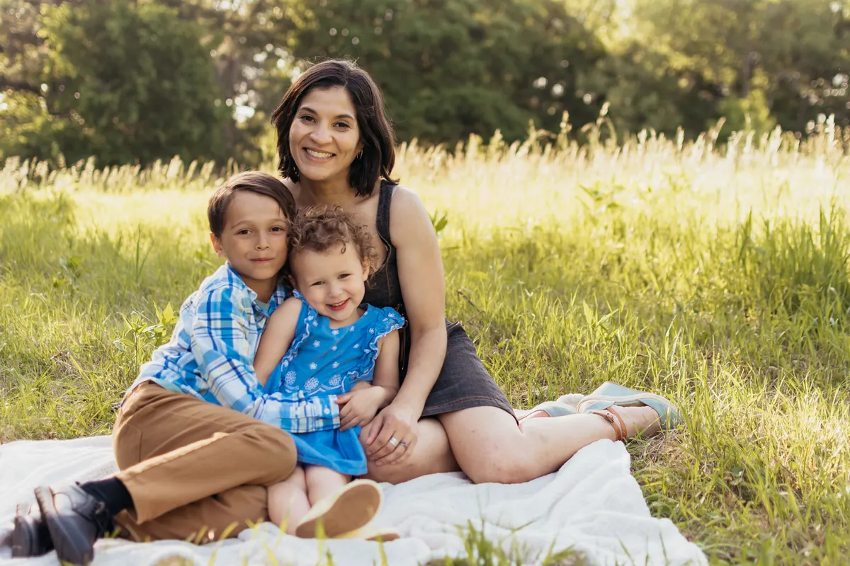 Mom sitting with her son and toddler daughter on a blanket in tall grass