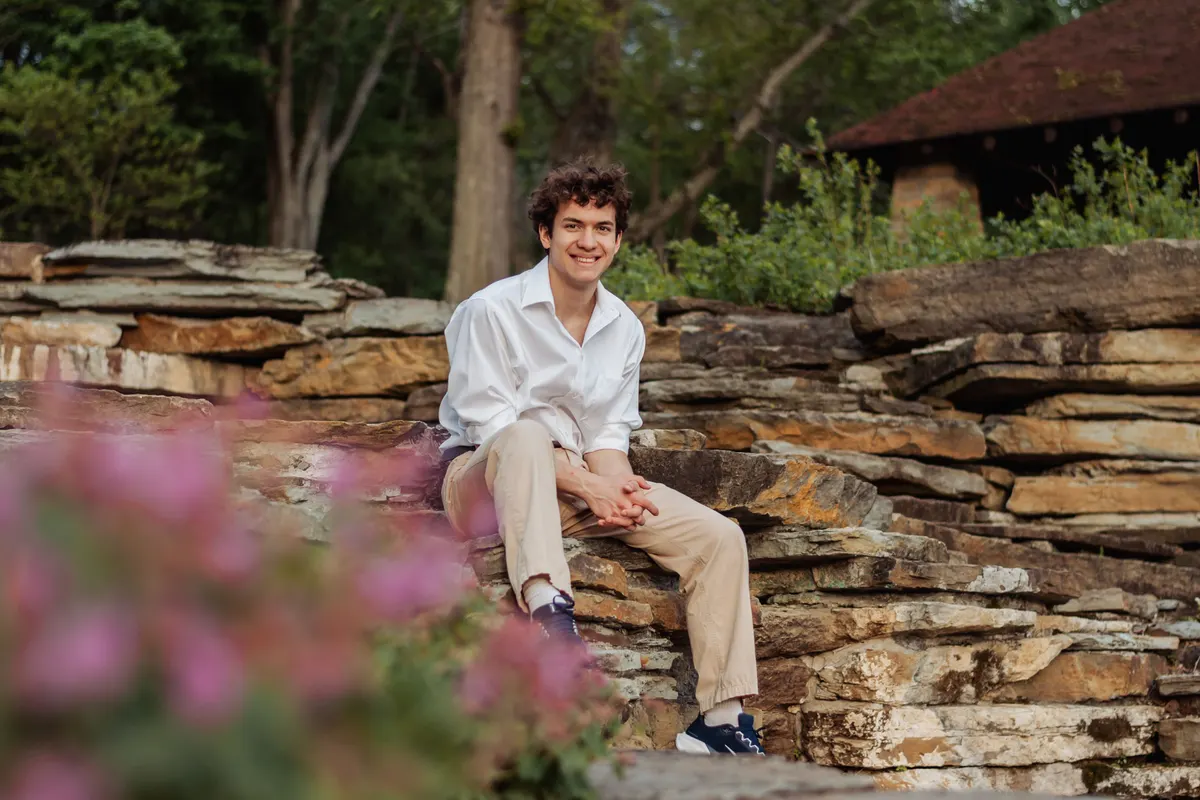 Senior boy sitting on a stone ledge behind spring blossoms at South Park
